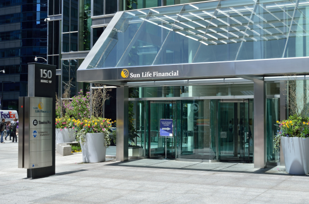 Modernes Glasgebäudes der Sun Life Financial in Toronto, Ontario, mit einem Schild, Topfpflanzen mit Blüten, Menschen, einem Straßenschild und Fahrzeugen an einem bewölkten Tag.
