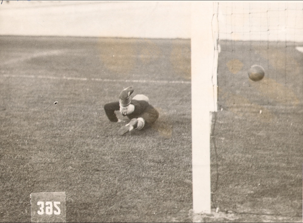 Ein Schwarz-Weiß-Foto eines Fussballspielers, der einen Ball vor einem Torpfosten mit Netz auf der rechten Seite fängt und Text unten.
